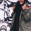 woman wearing olive green jacket in front of graffiti